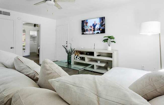 A living room with a white couch and a flat screen TV mounted on the wall.