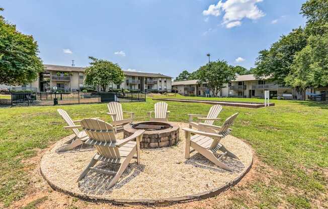 A fire pit surrounded by chairs in a grassy area.