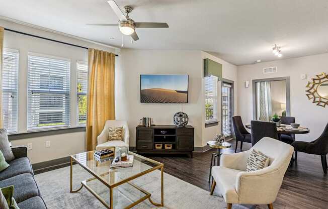 A living room with a grey sofa, a glass coffee table, a television, and a painting on the wall.