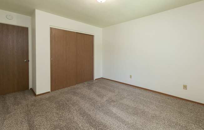 a bedroom with carpet and a door to a closet. Fargo, ND Islander Apartments