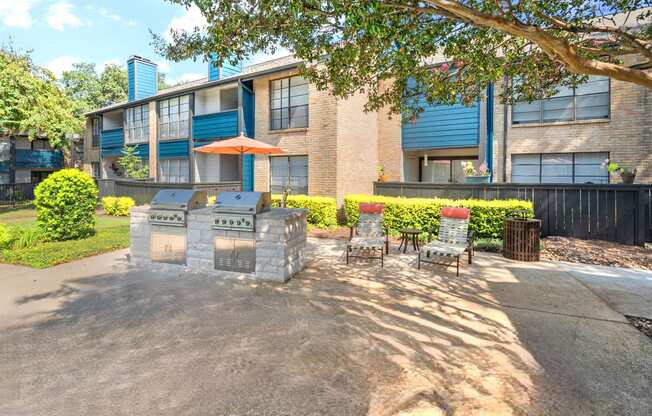 a patio with a grill and chairs in front of an apartment building