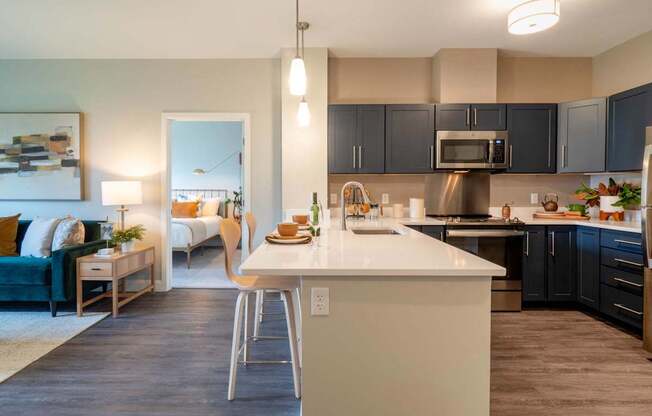 A sleek kitchen with quartz countertops, pendant lighting, and dark cabinetry equipped with stainless steel appliances.