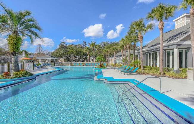 A large outdoor swimming pool surrounded by palm trees and lounge chairs.