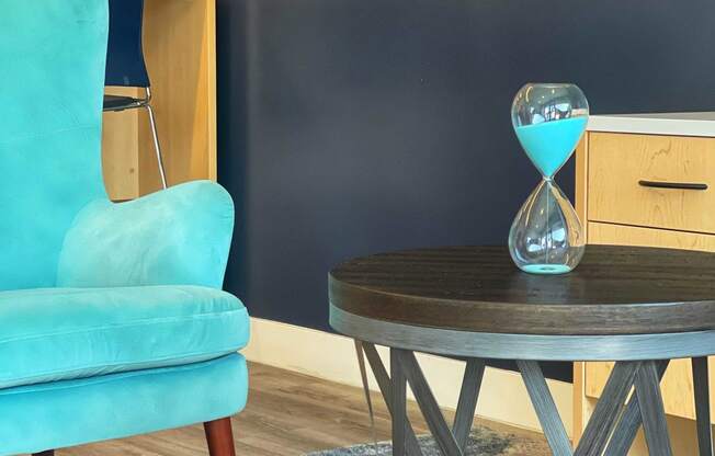 a blue chair and a round table with an hourglass on it