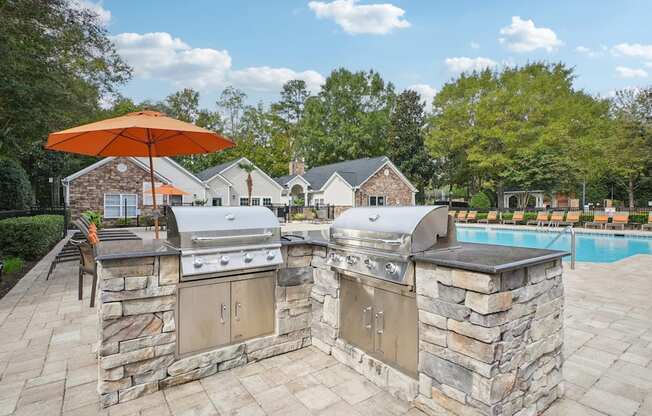 A stone outdoor kitchen with a grill and an orange umbrella.