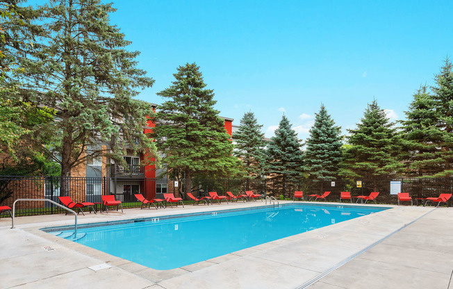 a swimming pool with red chairs around it in front of a building