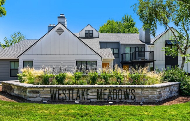 Two Bedroom Apartments in Lake Oswego, OR - Westlake Meadows - Property Entrance with Residential Buildings, Balconies, Landscaped Grounds, Mature Trees, and a Monument Sign.