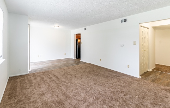 the living room and dining room of an apartment with carpeting and white walls