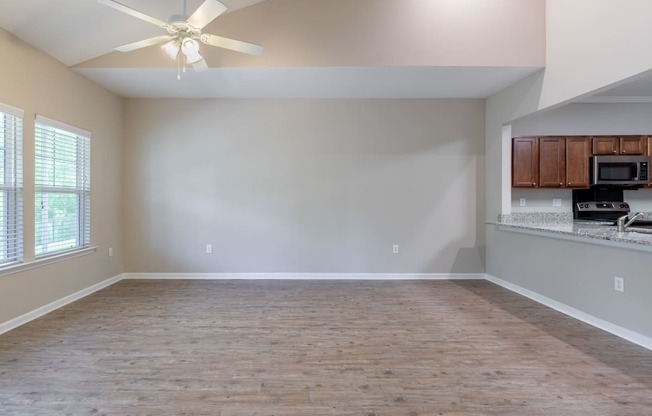 an empty living room with a kitchen and a ceiling fan