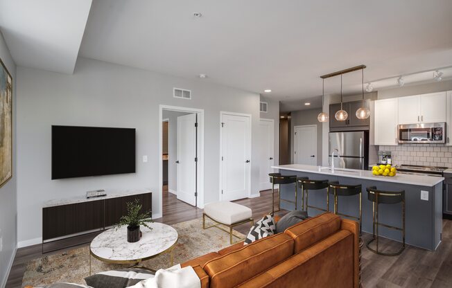 a living room with a couch and a table with three stools in front of a kitchen