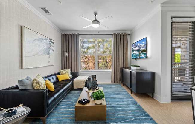 A living room with a black couch and a blue rug.