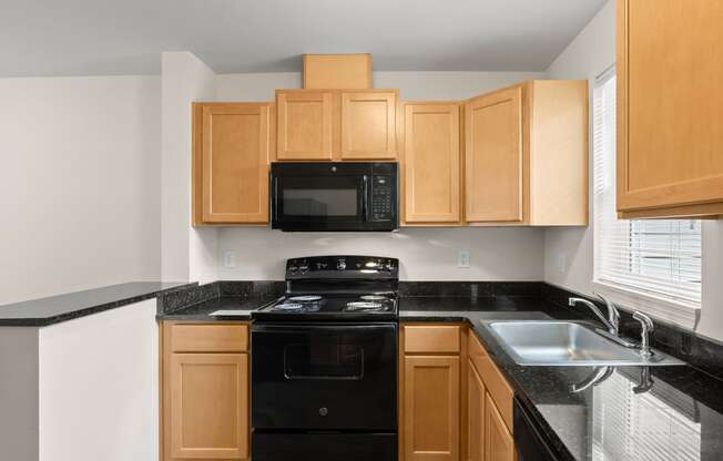 a kitchen with wood cabinets and black counter tops and black appliances