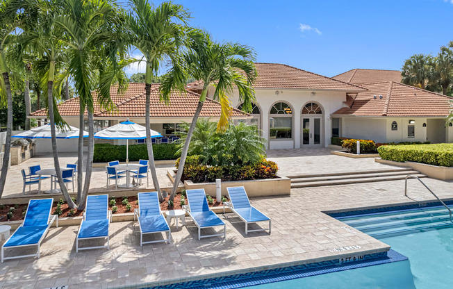 A pool area with sun loungers and a building in the background.