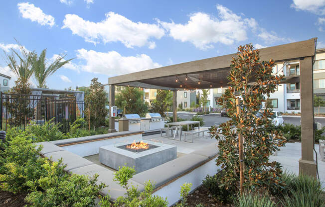 A patio with a fire pit surrounded by plants.