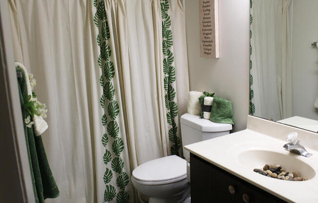 a bathroom with a white toilet next to a white sink with a green and white shower curtain