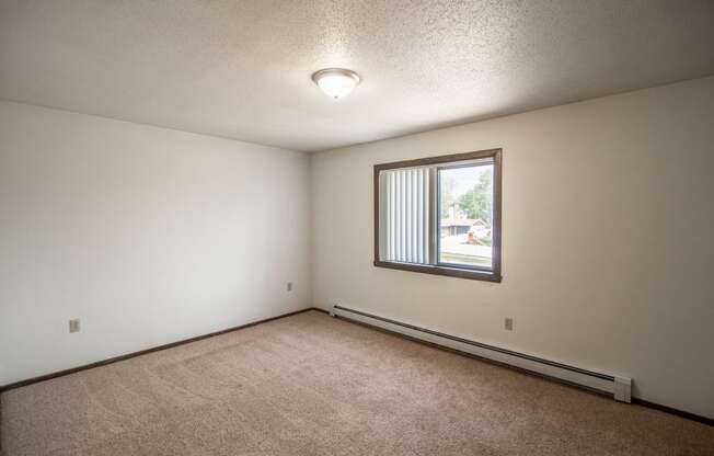 Bismarck, ND Rosser Apartments. a bedroom with a large window and beige carpet