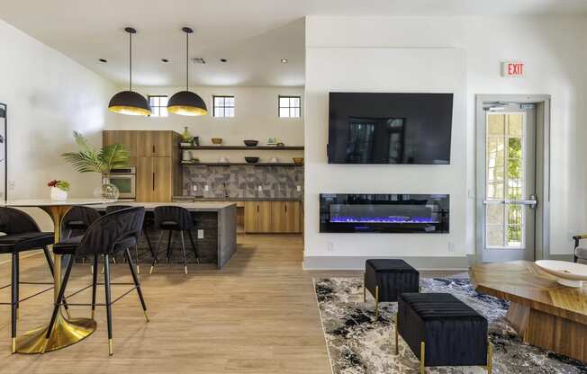 a living room with a large tv and a kitchen with a bar and stools