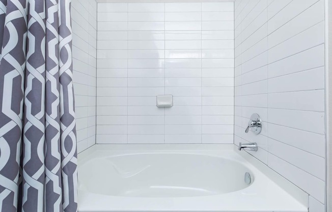 A white bathtub with a grey and white patterned shower curtain.
