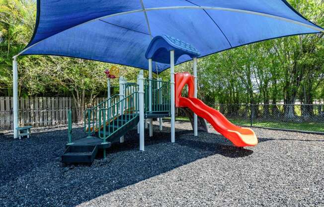 Apartments In Coconut Creek for Rent – Waterview at Coconut Creek – playground with a slide and a swing set under a blue umbrella