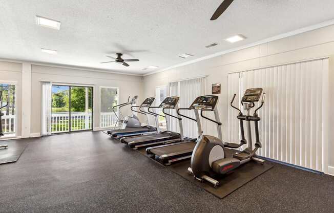 a gym with cardio machines and a ceiling fan