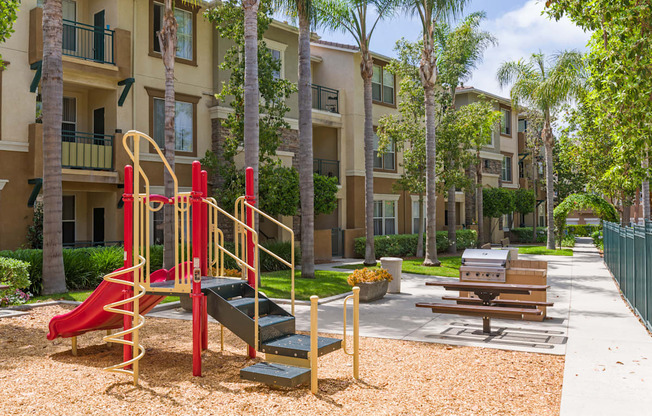 A playground with a red slide and a yellow slide in front of apartment buildings.
