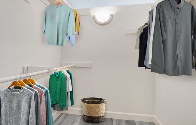 a walk in closet with clothes hanging on the wall