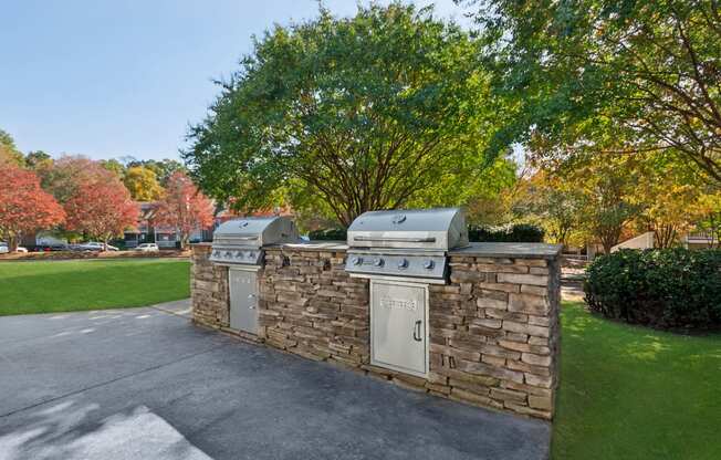 two gas barbecue grills on a stone wall in a driveway