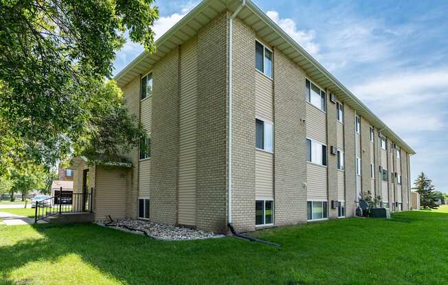 a brick building with green grass and a tree. Fargo, ND Park Circle Apartments.