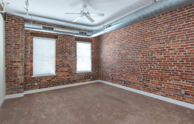 an empty room with a brick wall and a ceiling fan at Mayton Transfer Lofts, Petersburg, 23803