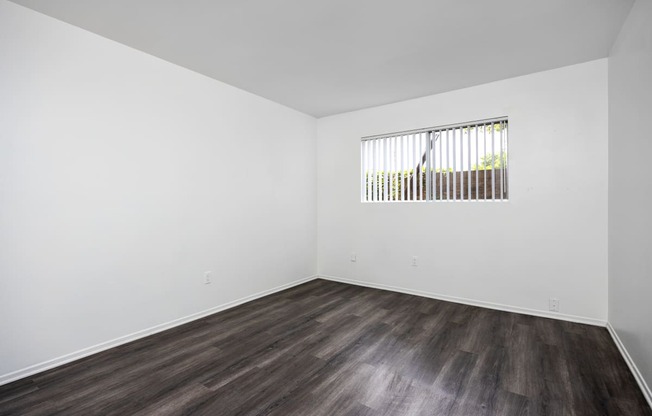 an empty room with white walls and wood floors and a window