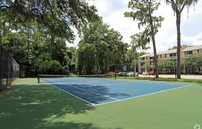 A tennis court surrounded by trees and a fence.