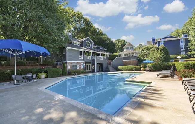 A large swimming pool in front of a house with a blue umbrella.