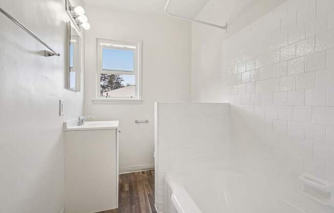 A white bathroom with a window and a tub.
