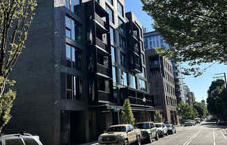 A street view of a row of modern buildings with cars parked on the side.