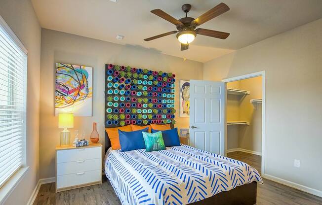 A bedroom with a bed, a ceiling fan, and a wall hanging.