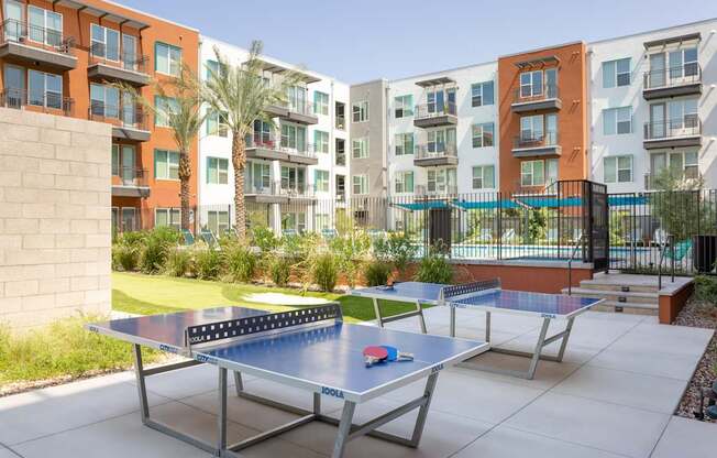 A ping pong table is in the middle of a courtyard with apartment buildings in the background.