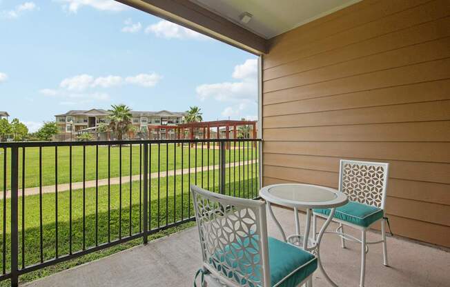 A patio with a table and chairs overlooking a grassy area.
