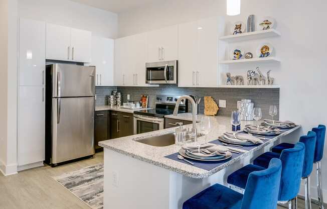 a kitchen with white cabinets and a large island with a granite countertop and blue chairs