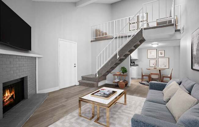 A living room with a grey couch, a coffee table, a fireplace, and a staircase.