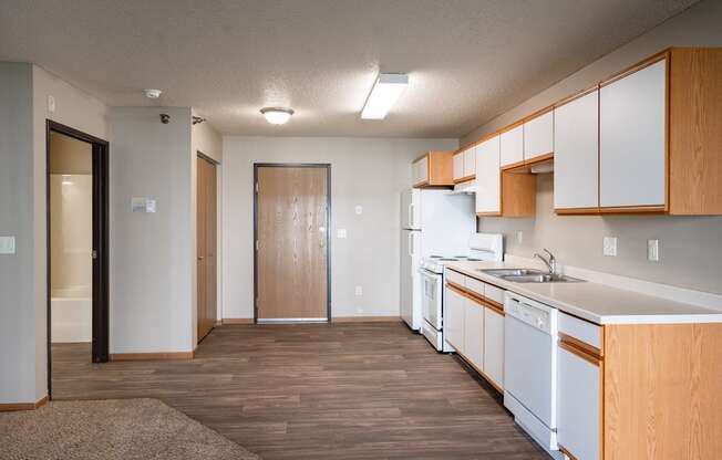 an empty kitchen with white appliances and wood flooring and a door to the bathroom