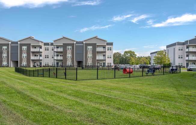 A row of apartment buildings with a grassy field in front and cars parked in the background.