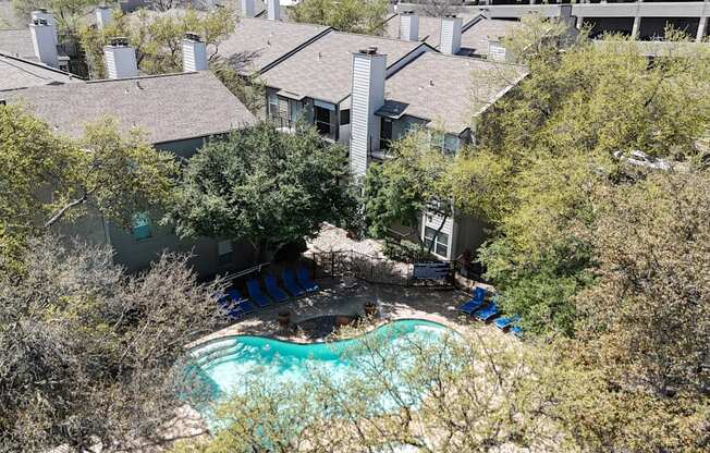 A swimming pool surrounded by lush trees and apartment buildings at The Park on Preston Apartments in Dallas, TX