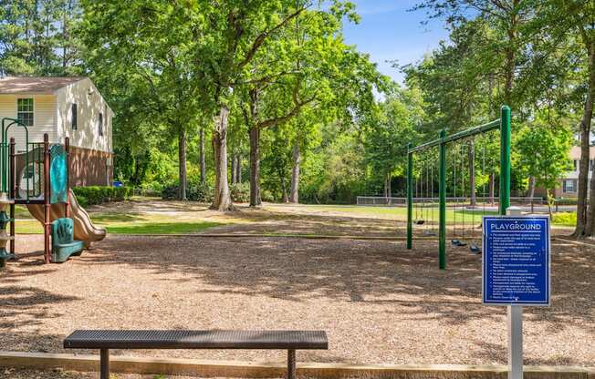 A playground with a sign that says "PLAYGROUND" in the middle of a wooded area.