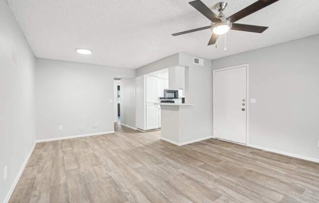 A room with a ceiling fan and light fixture, and a kitchenette in the corner.
