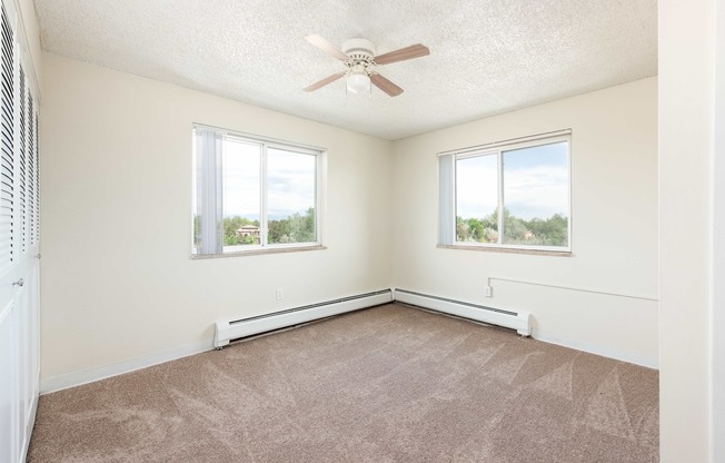 an empty bedroom with a ceiling fan and two windows