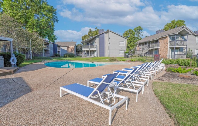 A sunny day at the pool with lounge chairs and apartments in the background at Laurel Parc apartments in Shreveport, LA.