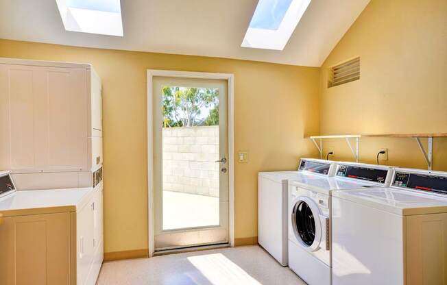 A laundry room with a washer and dryer, a door leading outside, and a skylight.