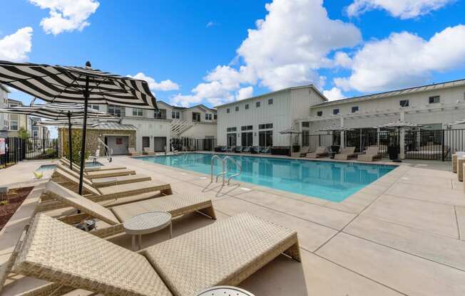 Outdoor pool area with tan colored lounge seating and black & white pool-side umbrellas at Morgan Ranch Apartments, Morgan Hill, California