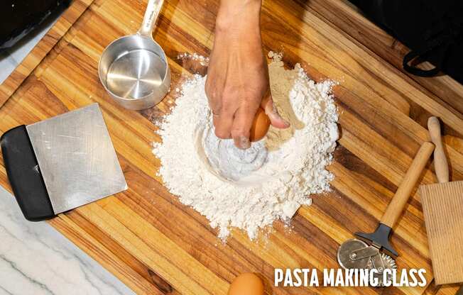 A person is making pasta with a metal scoop and a wooden spatula on a wooden board.