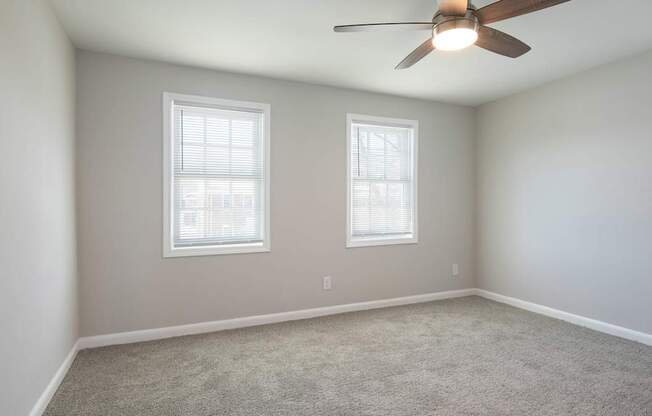 A room with a ceiling fan and two windows.